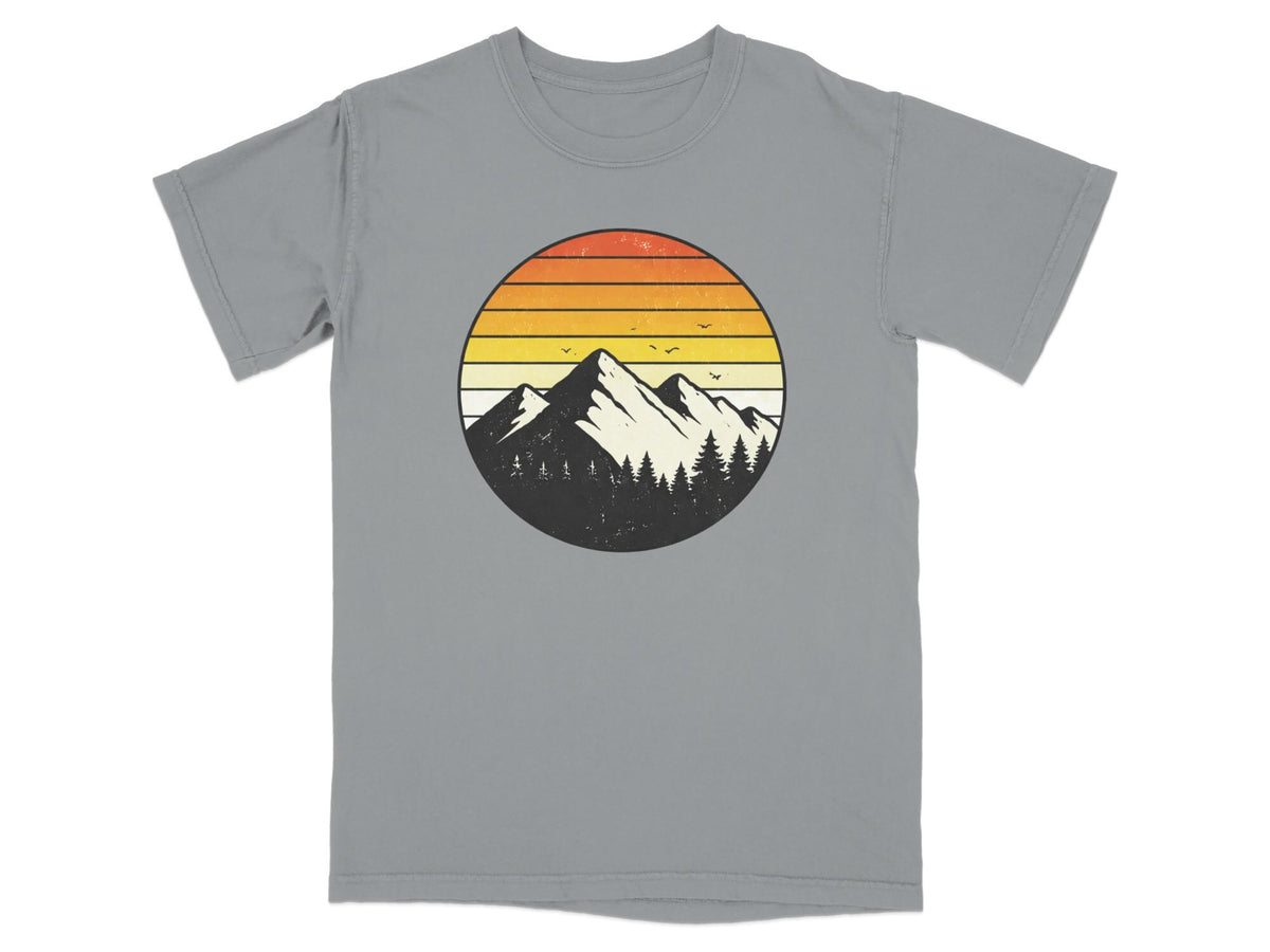 Circular graphic of mountains and trees against a sunset on a gray t-shirt.