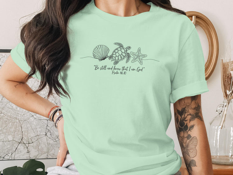 Light green t-shirt with shell, starfish, and turtle line art and Bible verse.