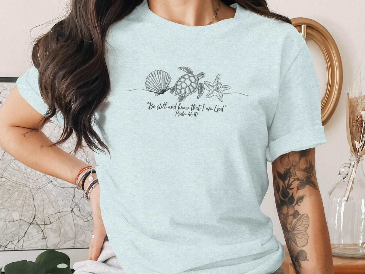 Light blue t-shirt with seashell, starfish, and turtle line art and "Be still and know that I am God" text.