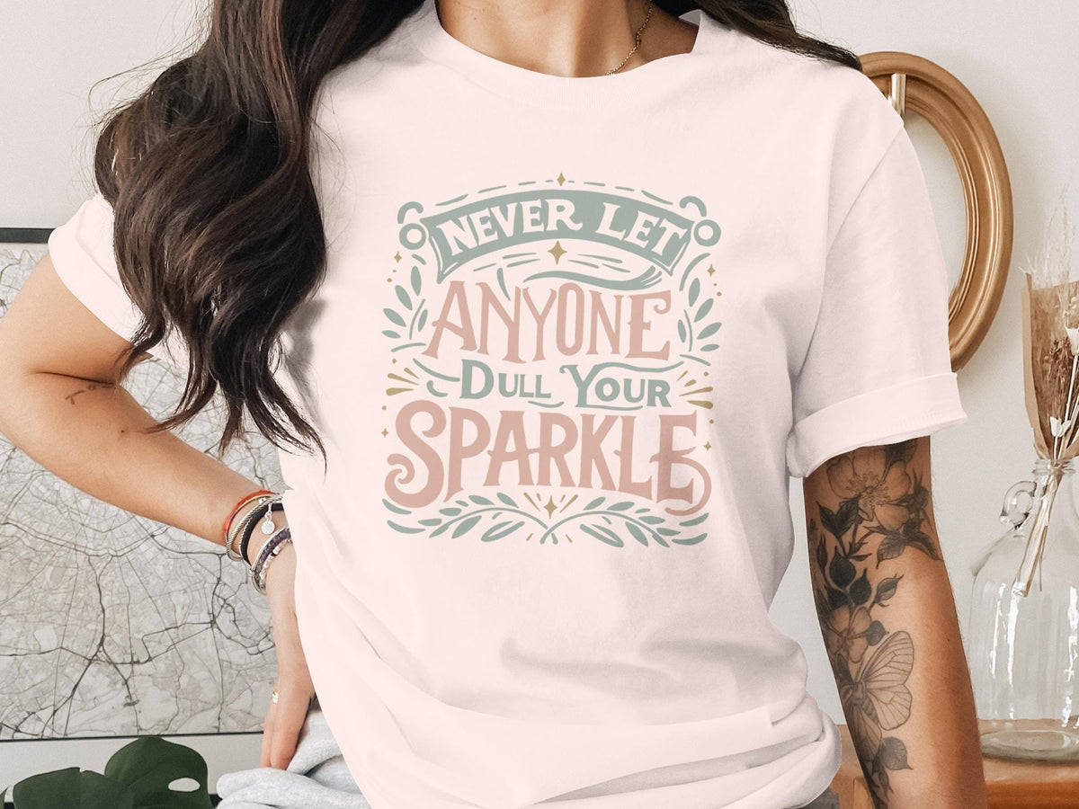 "Never let anyone dull your sparkle" text on a light pink t-shirt.