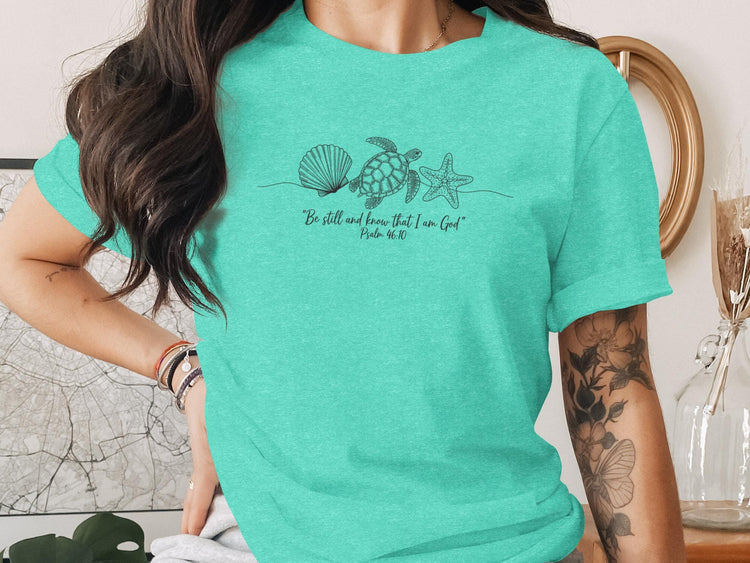 Teal t-shirt with line art of shell, starfish, and turtle, "Be still and know that I am God".