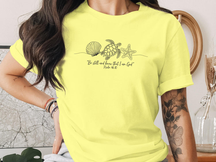 Yellow t-shirt with line art seashell, starfish, and turtle, with text "Be still and know that I am God".
