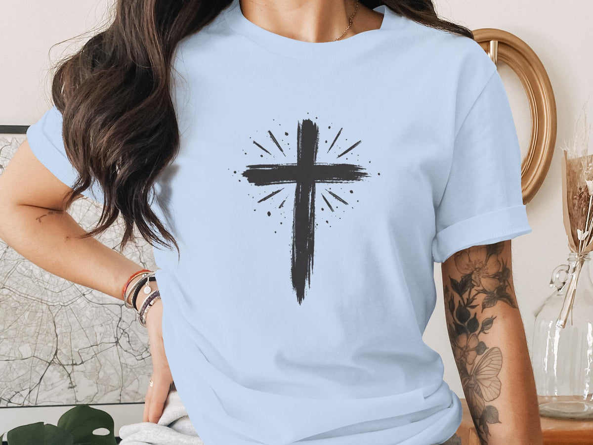 Black painted cross with radiating lines on a light blue t-shirt.
