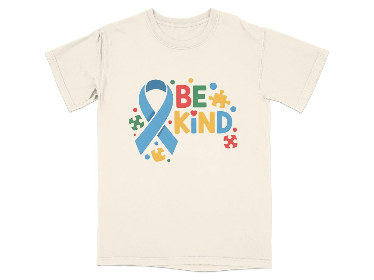 Cream t-shirt with blue ribbon and "BE KIND" text surrounded by colorful puzzle pieces.