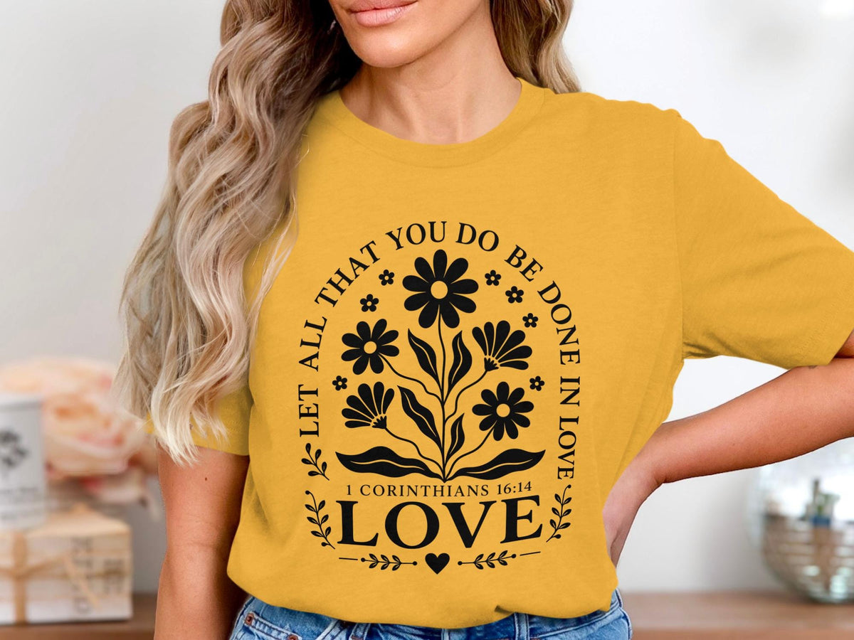 Yellow t-shirt with black floral design and text "LET ALL THAT YOU DO BE DONE IN LOVE LOVE 1 CORINTHIANS 16:14".