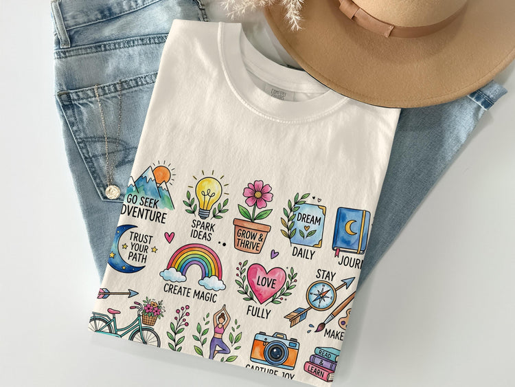Flat lay of a cream t-shirt with watercolor illustrations of adventure and self-care icons.
