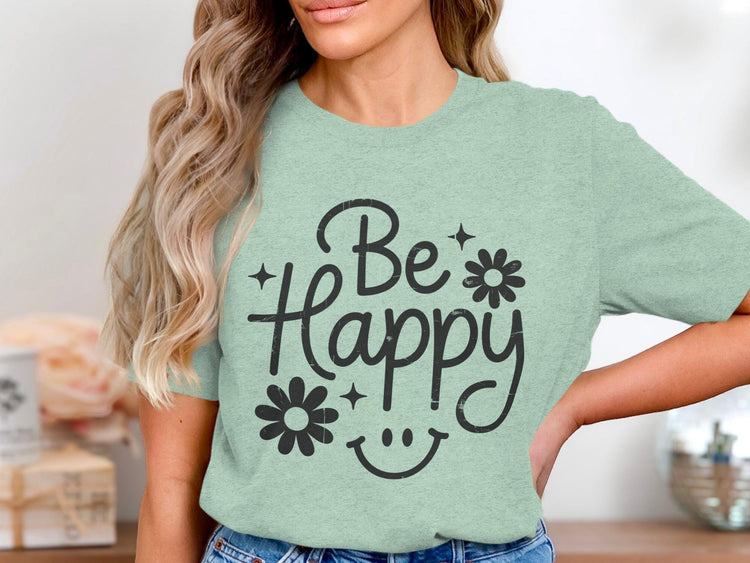 Woman wearing a light green t-shirt with "Be Happy" text, flowers, stars, and smiley face.