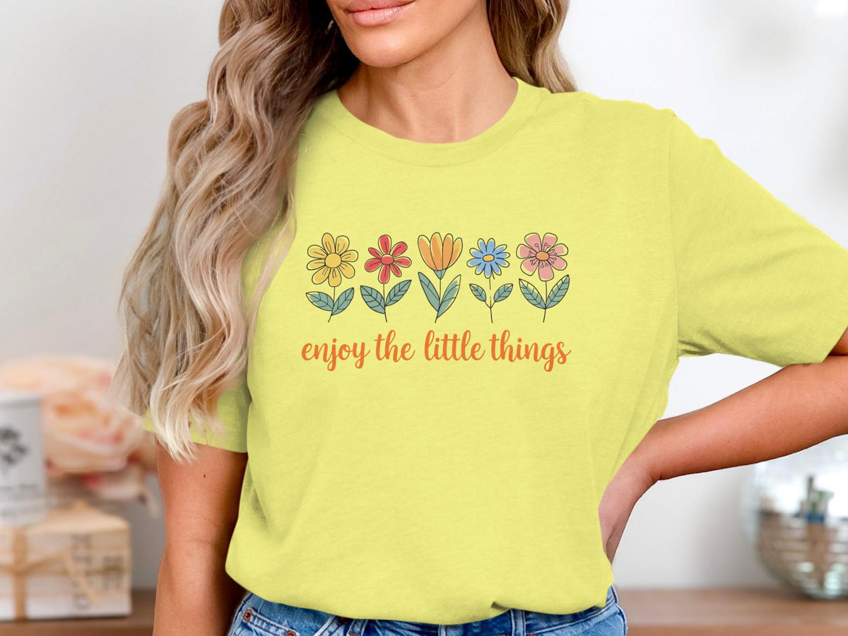 Yellow t-shirt with a line of colorful cartoon flowers and the text "enjoy the little things".