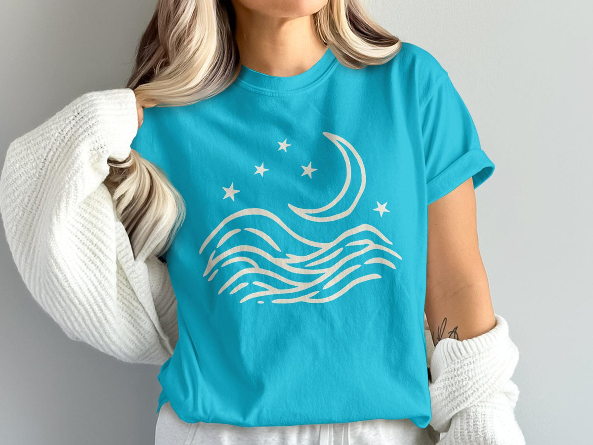 Turquoise t-shirt with moon, stars, and wavy lines graphic design.
