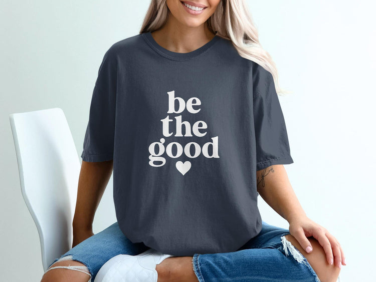 Dark gray t-shirt with white text "be the good" and a small heart.