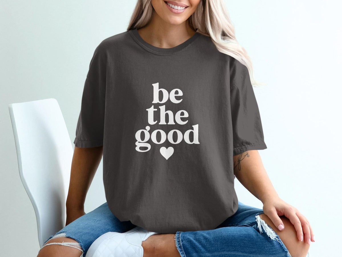 Dark grey t-shirt with white text "be the good" and a heart symbol.
