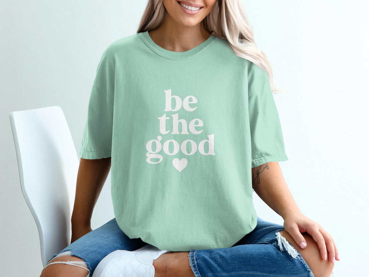 Mint green t-shirt with white text that reads "be the good" and a heart accent.