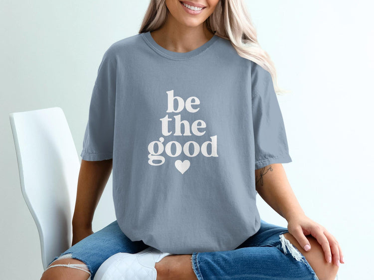 Blue t-shirt with white text reading "be the good" and a heart.