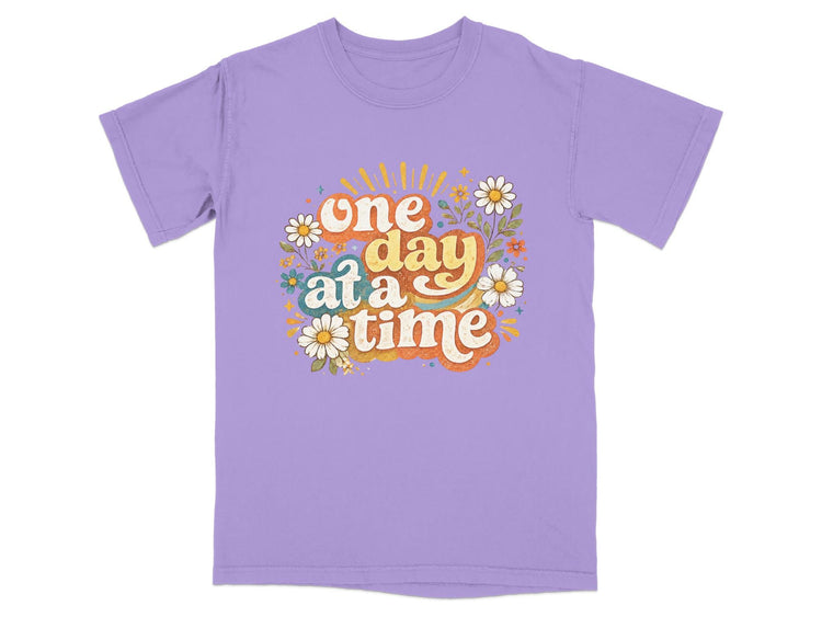 Purple t-shirt with "one day at a time" text surrounded by retro flowers.