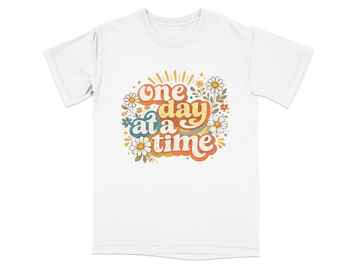 White t-shirt with "one day at a time" text and floral design.