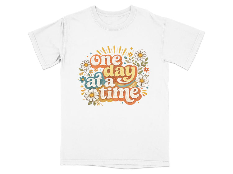 White t-shirt with "one day at a time" text and floral design.
