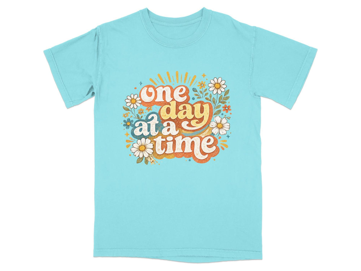 Blue t-shirt with "one day at a time" text and floral graphics.