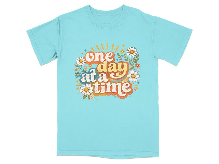 Blue t-shirt with "one day at a time" text and floral graphics.