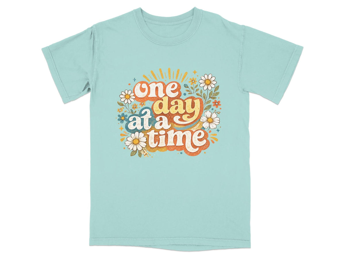 Aqua t-shirt with "one day at a time" text and floral graphics.