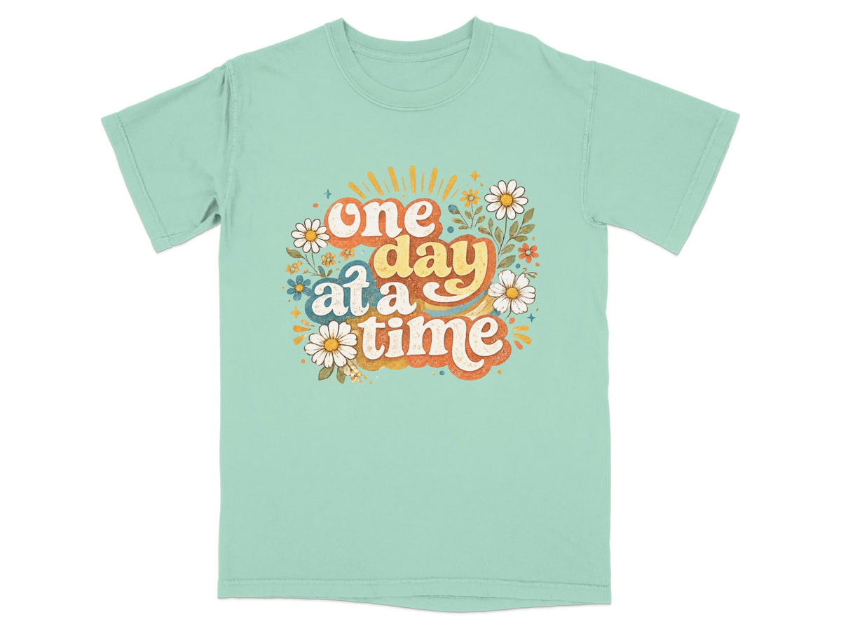 Teal t-shirt with colorful "one day at a time" graphic and flowers.