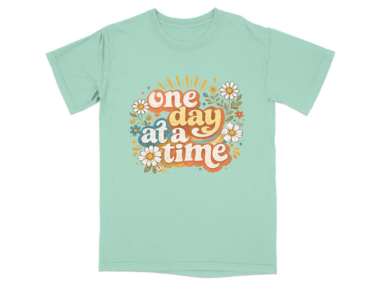 Teal t-shirt with colorful "one day at a time" graphic and flowers.