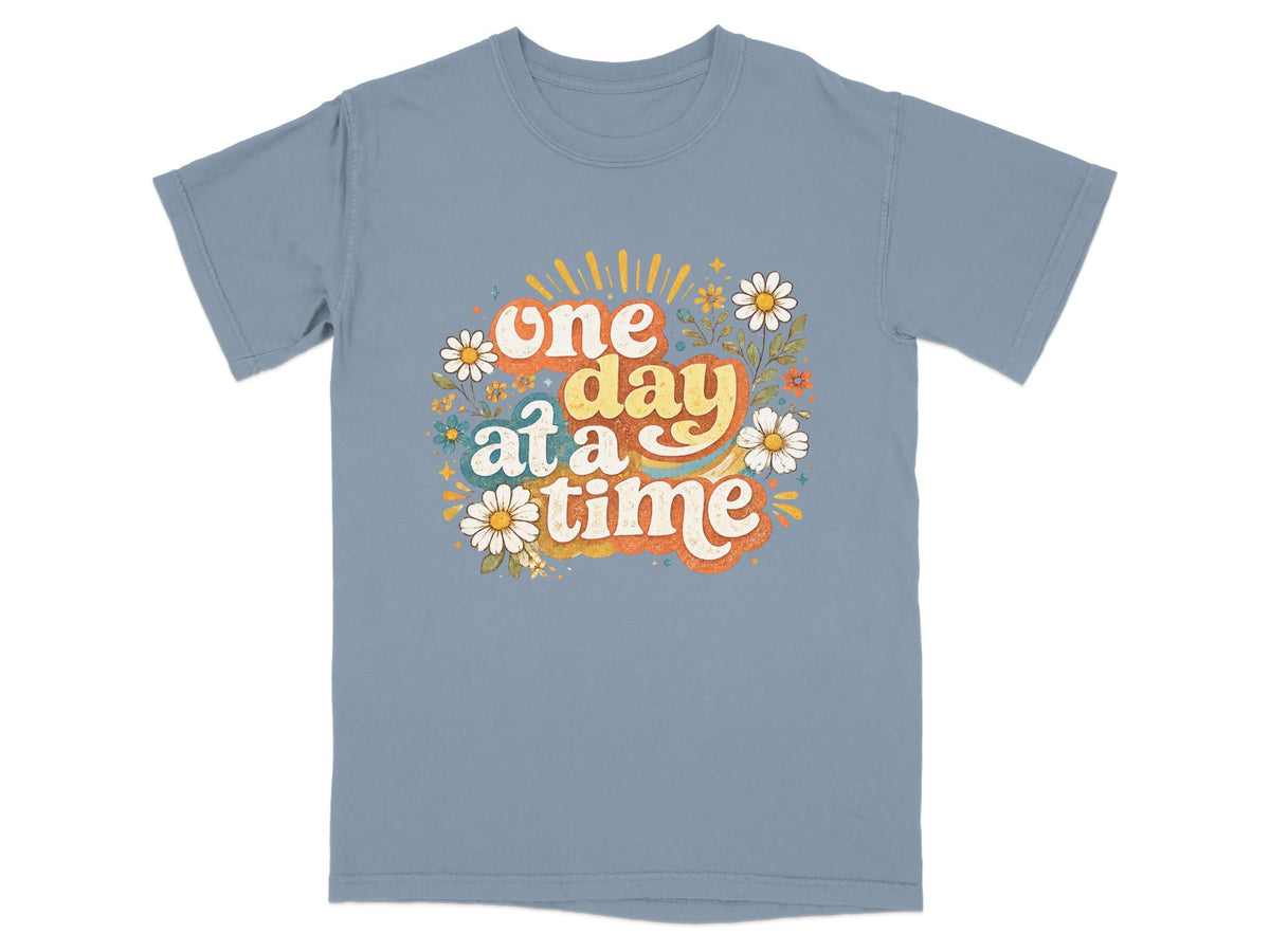 Blue t-shirt with "one day at a time" text and retro floral design.