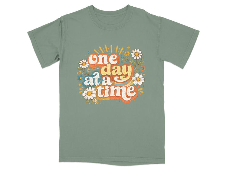 Green t-shirt with "one day at a time" text and floral graphics.
