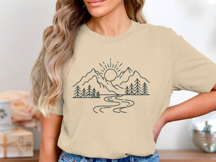 Line art of mountains, trees, river, and sunrise on a light tan shirt.
