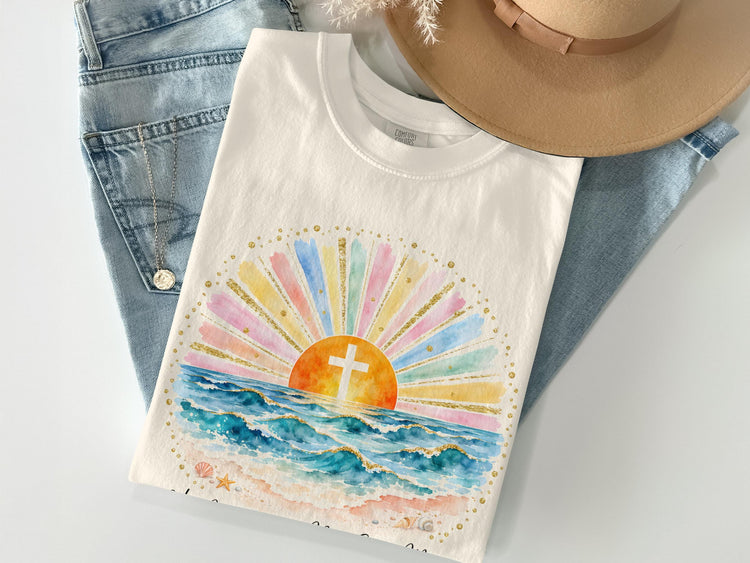 White t-shirt with watercolor beach sunrise and cross graphic, gold accents.