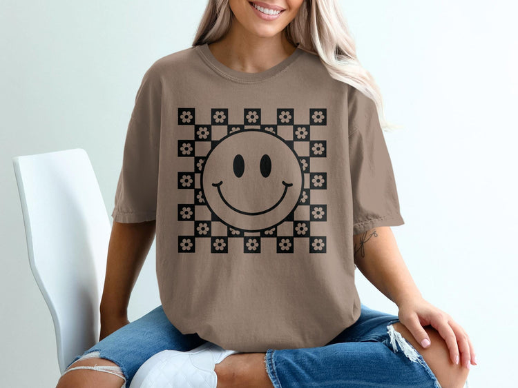 Brown t-shirt with a black smiley face and floral checkerboard graphic.
