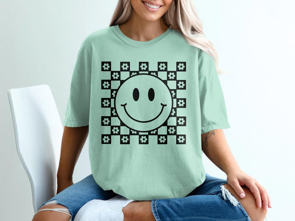 Light green t-shirt with black smiley face and checkerboard flower graphic.