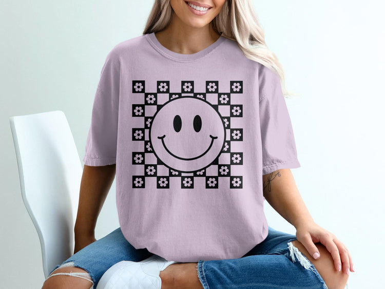 Lavender t-shirt with a black smiley face and floral checkerboard graphic.