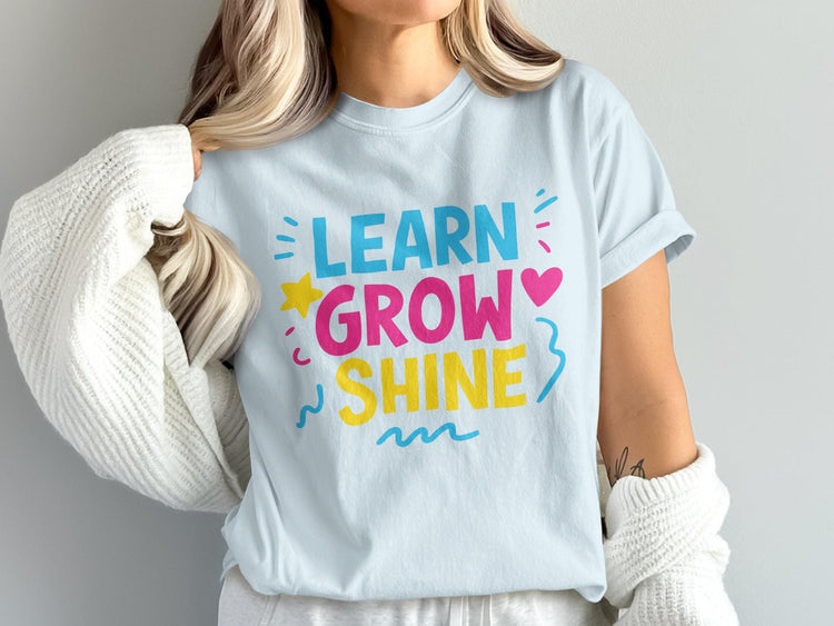 Light blue t-shirt with "LEARN GROW SHINE" text in bright blue, pink, and yellow.