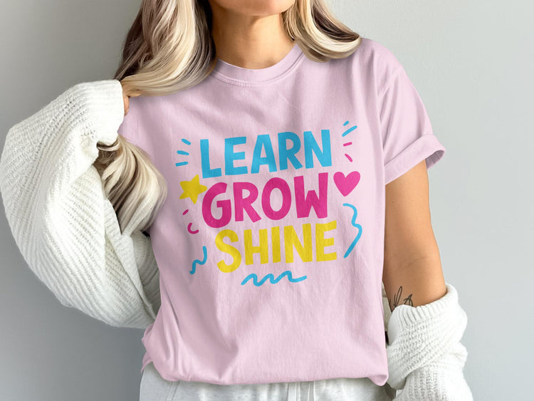 Pink t-shirt with "LEARN GROW SHINE" text in colorful letters and playful graphics.