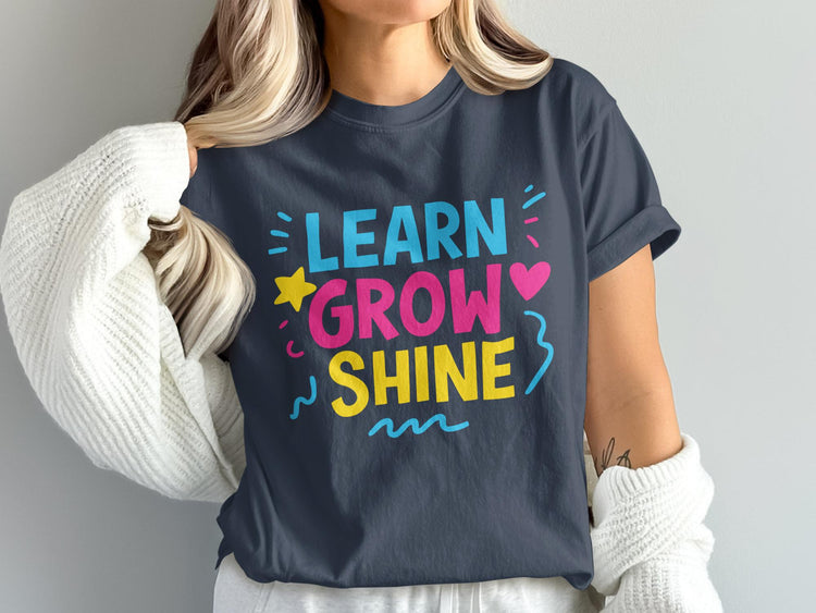 Dark t-shirt with "LEARN GROW SHINE" in colorful block letters with decorative elements.