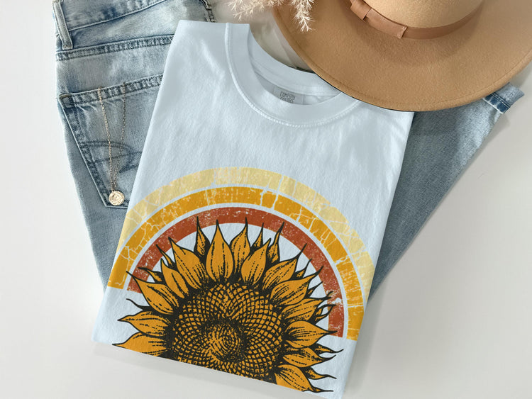 Light blue t-shirt with a distressed sunflower and concentric rainbow graphic.