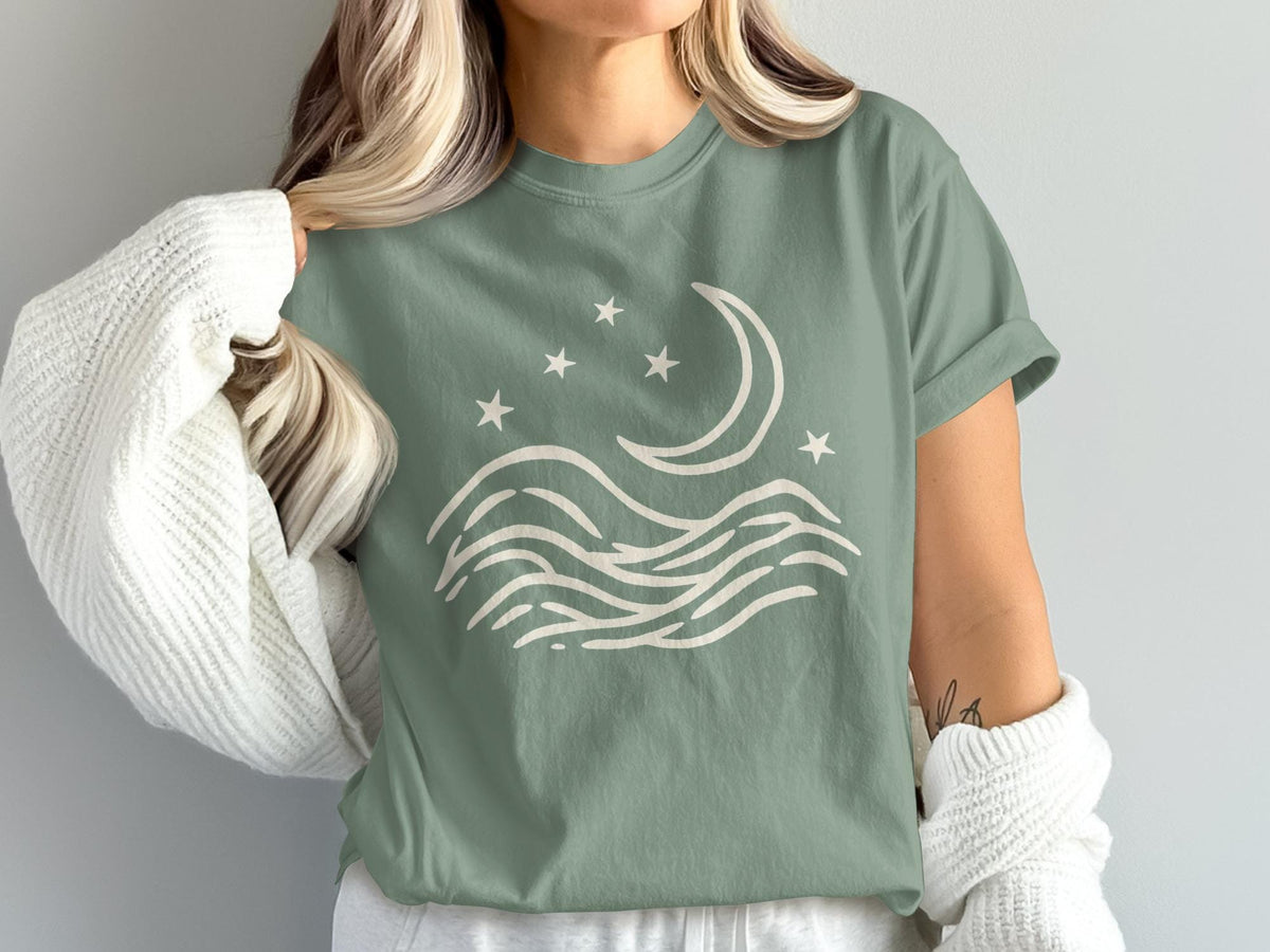 Sage t-shirt with a cream graphic of a crescent moon, stars, and waves.