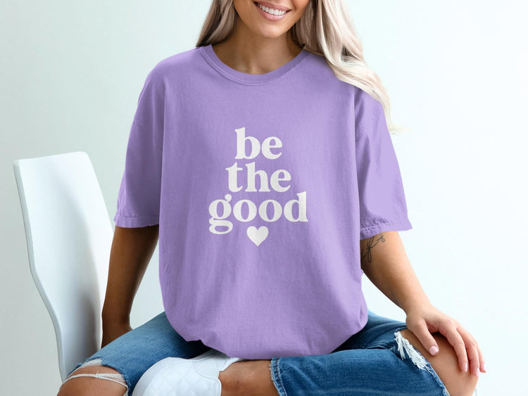 Purple t-shirt with white text "be the good" and a heart graphic.