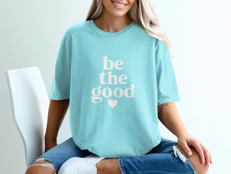 Teal t-shirt with white "be the good" text and a heart graphic.