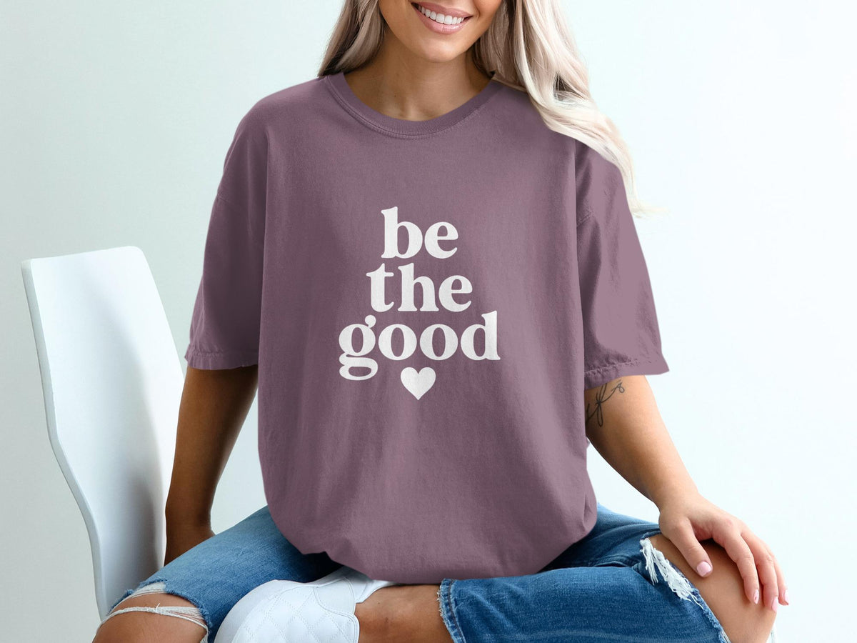 Purple t-shirt with white text "be the good" and a heart.