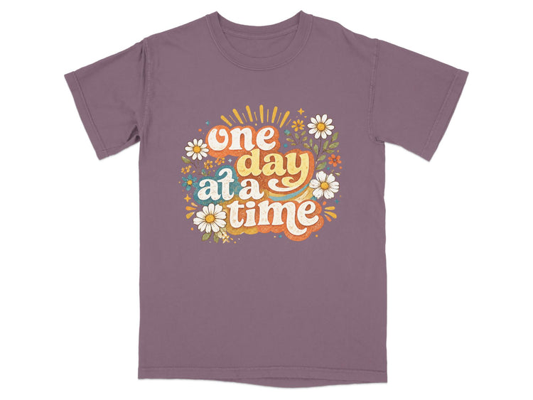 Purple t-shirt with "one day at a time" text and floral design.