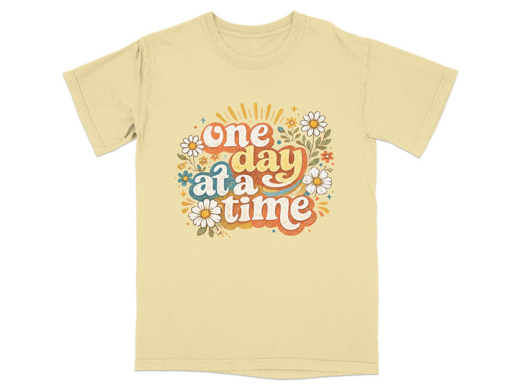 Yellow t-shirt with "one day at a time" text surrounded by flowers and stars.