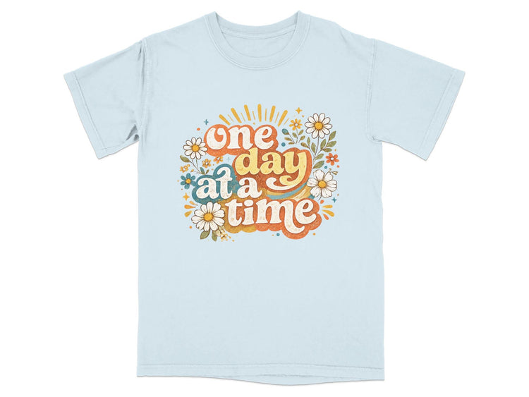 Light blue t-shirt with retro floral graphic saying "one day at a time"