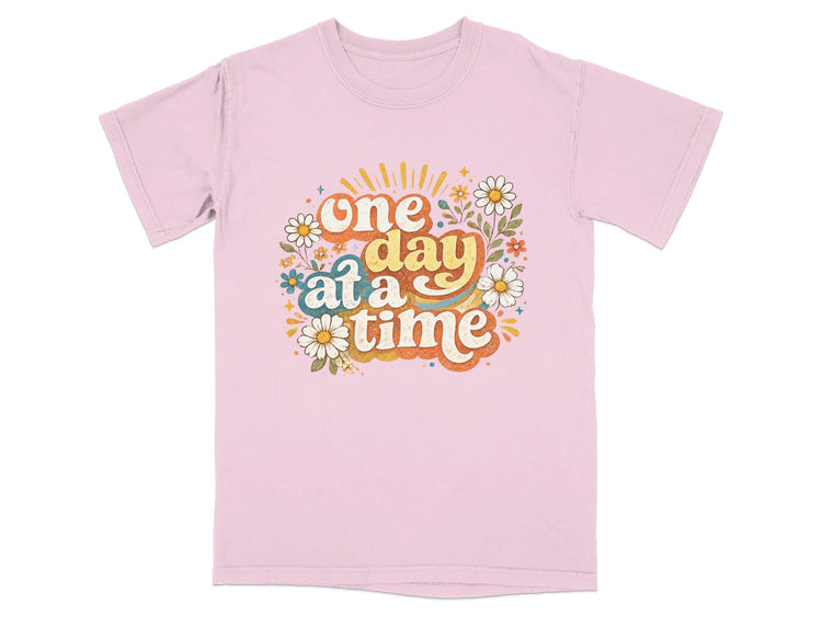 Pink t-shirt with "one day at a time" text and floral graphic.