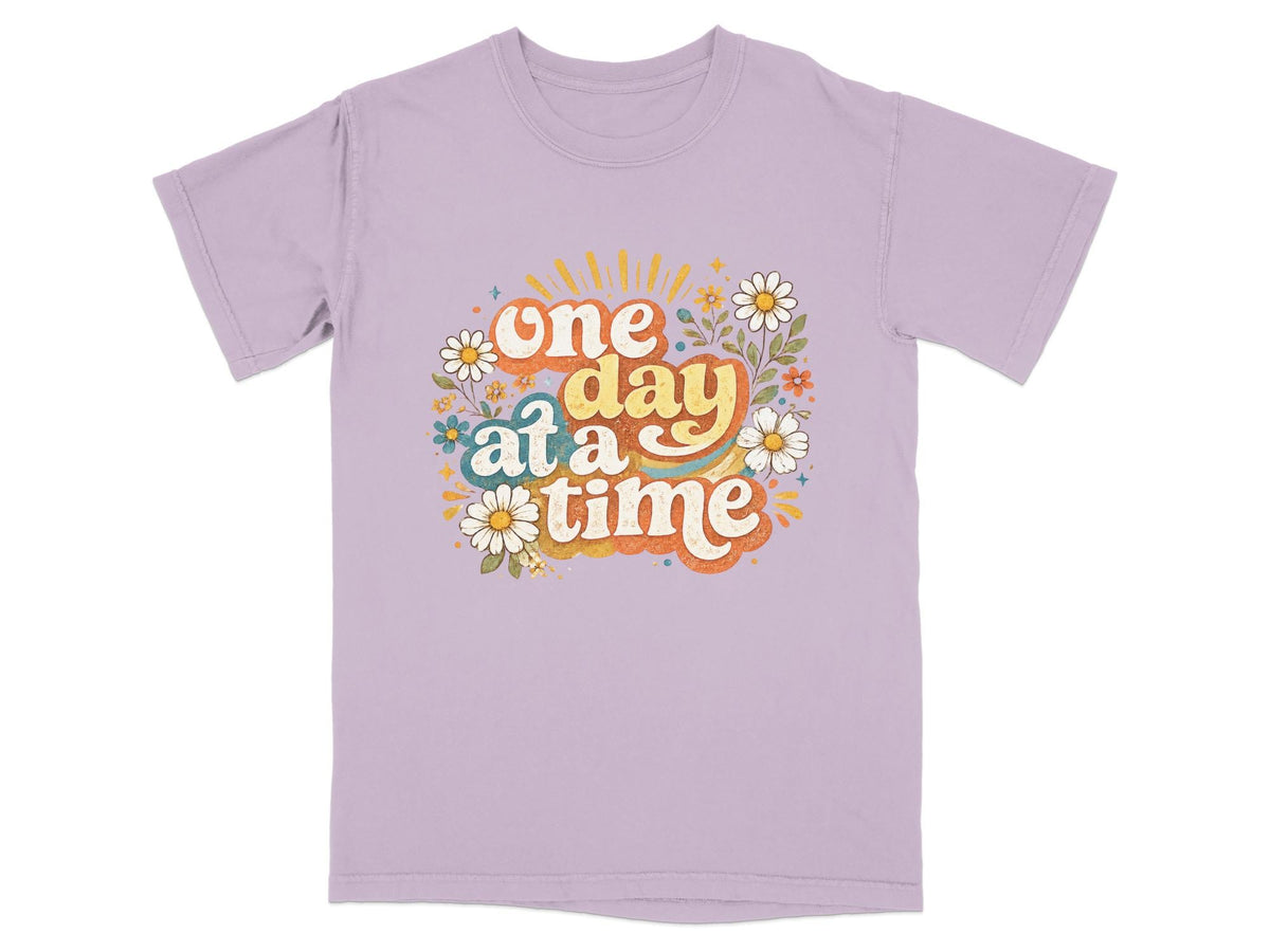 Purple t-shirt with "one day at a time" text and floral graphic.