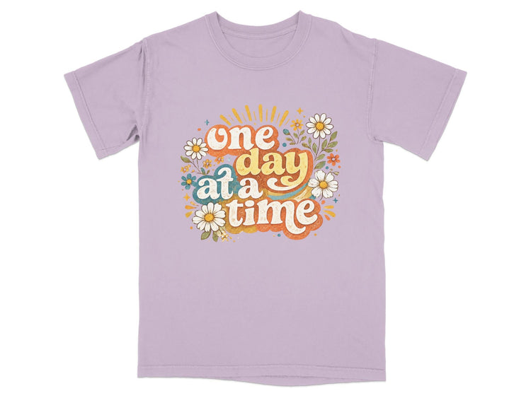 Purple t-shirt with "one day at a time" text and floral graphic.