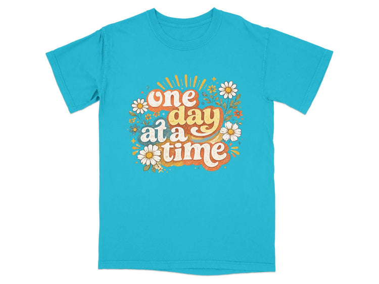 Turquoise t-shirt with "one day at a time" text and floral design.