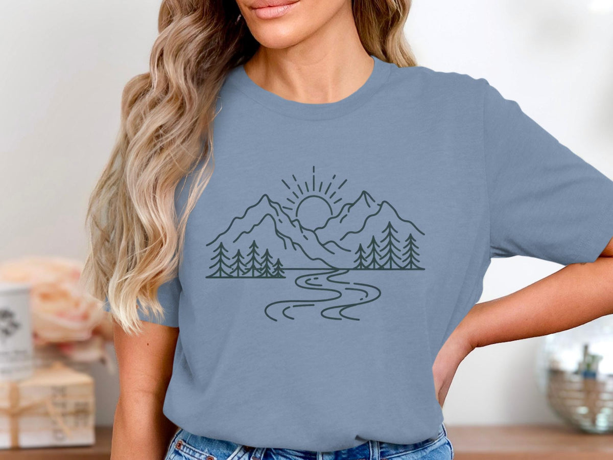 Line art design of mountains, trees, river, and sun on blue t-shirt.