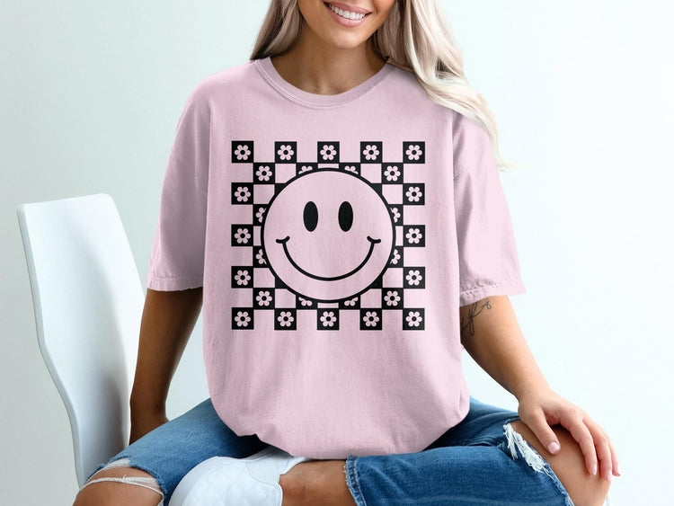 Pink t-shirt with a black smiley face on a checkerboard pattern with flowers.