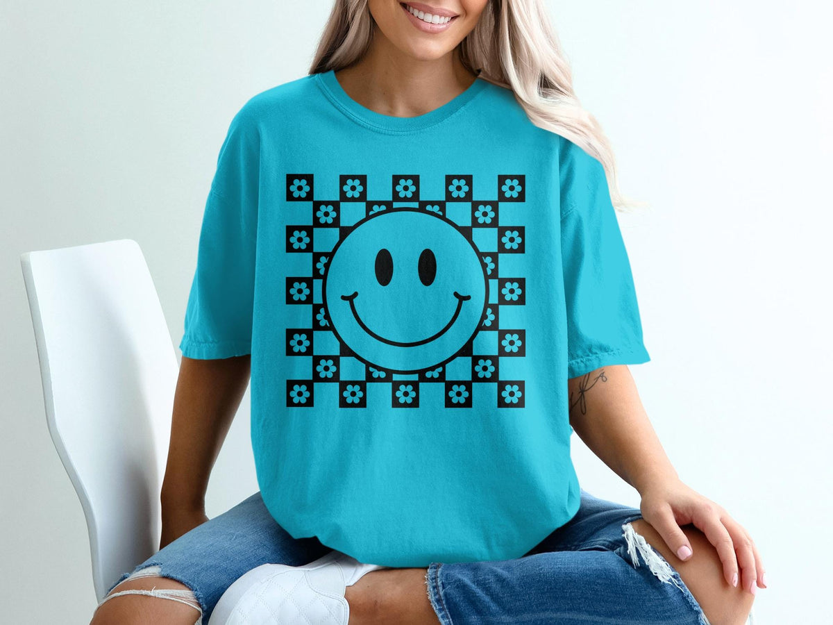 Teal t-shirt with a black checkerboard smiley face and flower graphic.